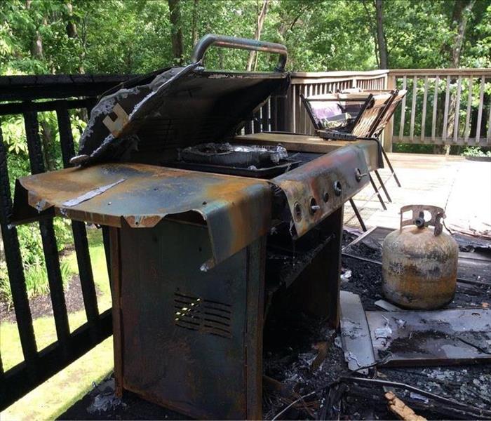 A photo of a melted grill on an outdoor deck. The whole space is charred and black.